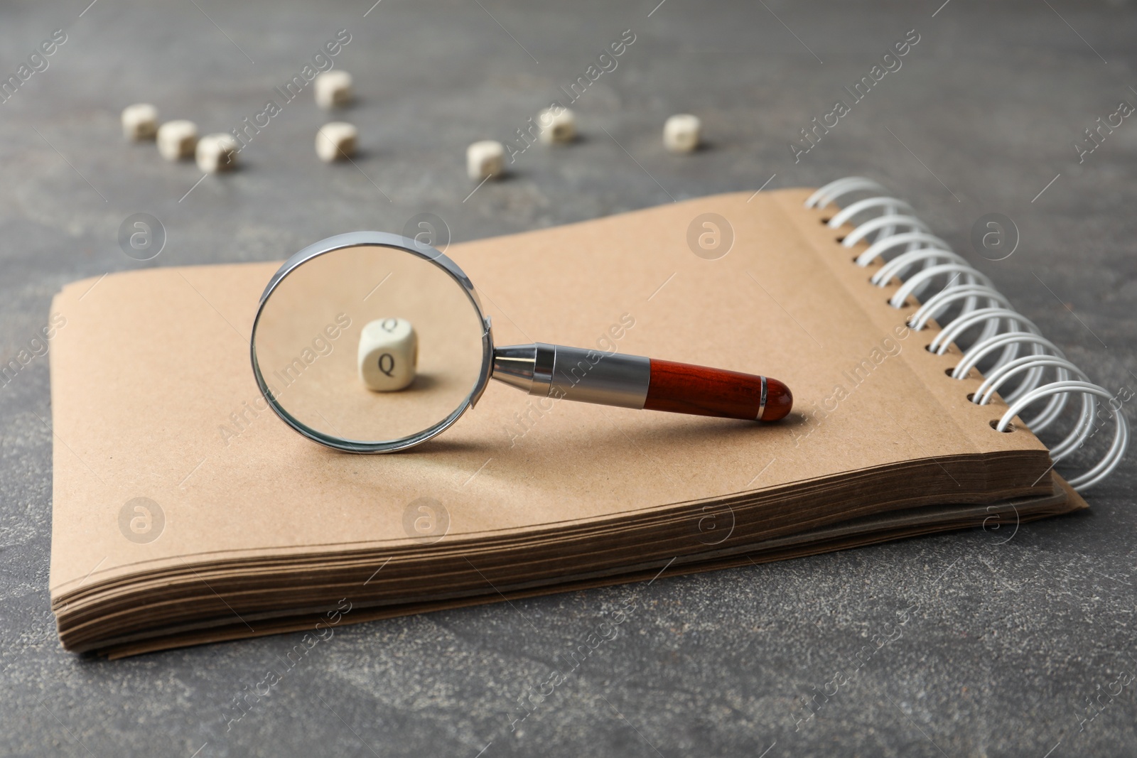 Photo of Magnifier glass, cube with letter Q and empty notebook on grey stone background, closeup. Find keywords concept