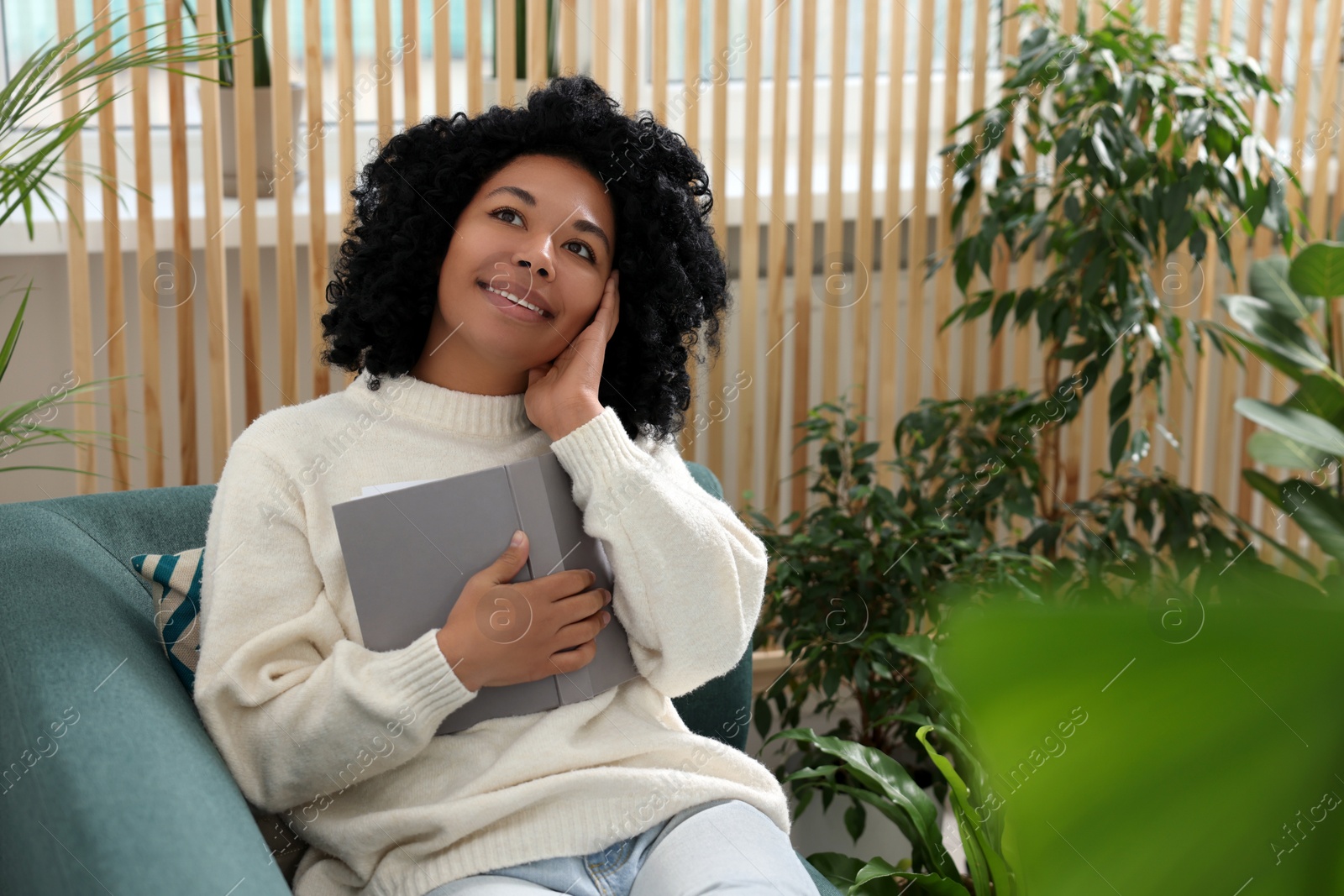 Photo of Relaxing atmosphere. Happy woman with book on sofa surrounded by beautiful houseplants in room