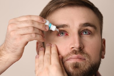 Image of Man using eye drops on beige background, closeup