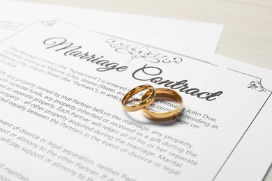 Photo of Marriage contracts and gold rings on light wooden table, closeup