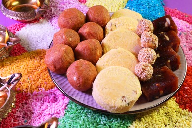 Diwali celebration. Tasty Indian sweets, colorful rangoli and diya lamps on table, closeup