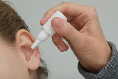 Mother dripping medication into daughter's ear on light grey background, closeup