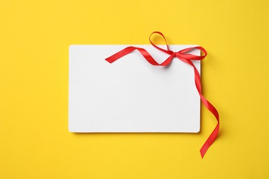 Blank gift card with red bow on yellow background, top view. Space for text