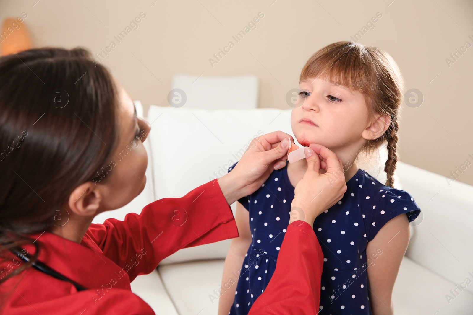 Photo of Nurse applying medical patch to little girl's injured face indoors. First aid