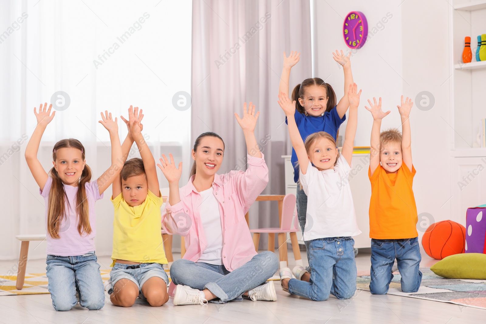 Photo of Nursery teacher and group of cute little children spending time together on floor in kindergarten. Playtime activities