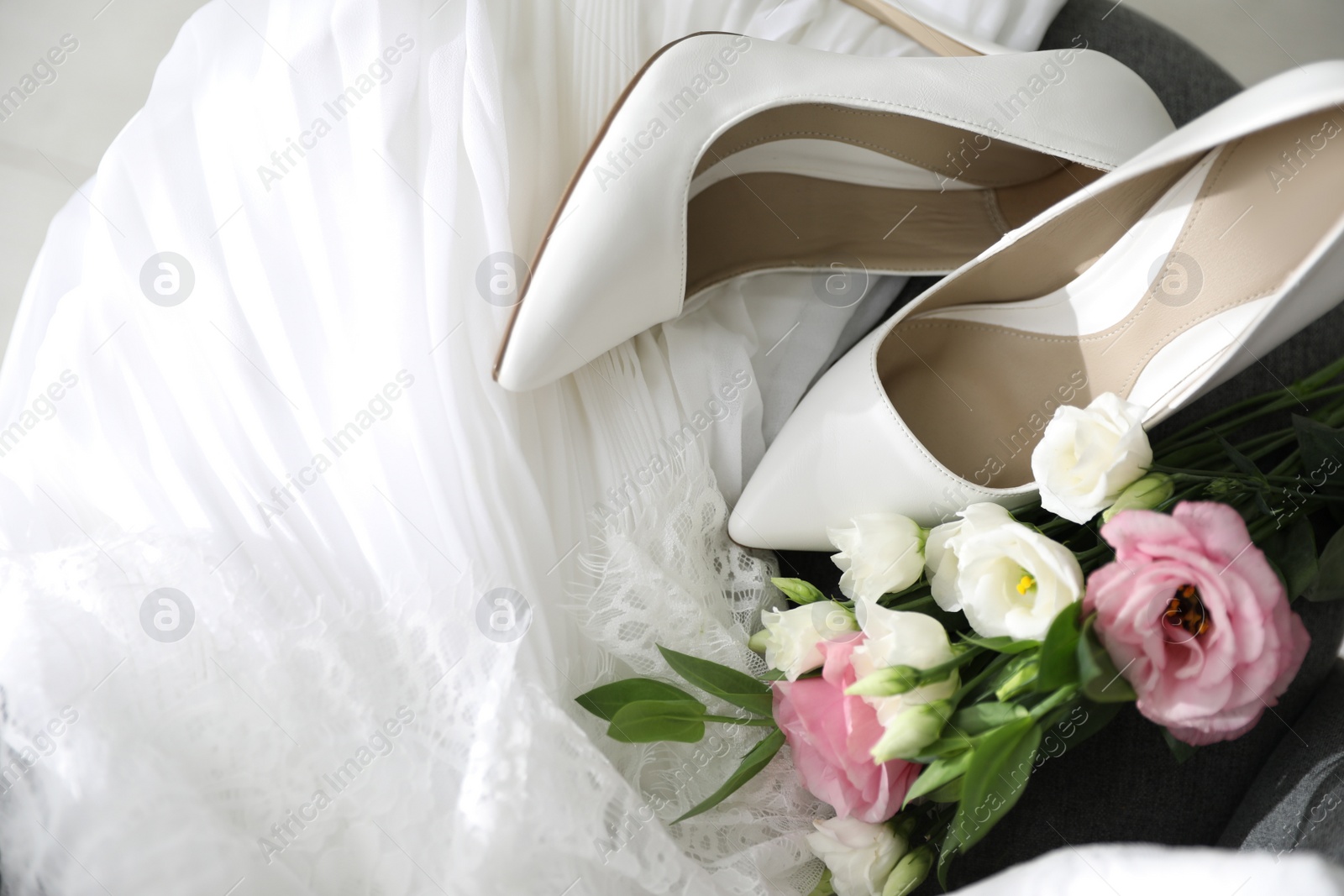 Photo of Pair of white high heel shoes, flowers and wedding dress, above view
