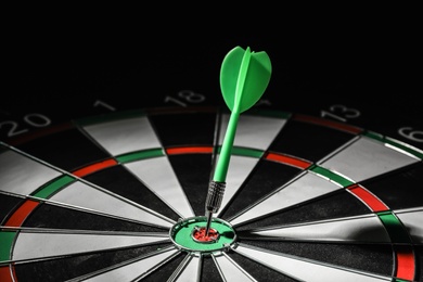 Photo of Green arrow hitting target on dart board against black background