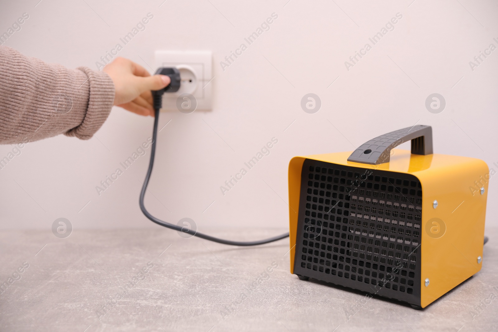 Photo of Woman plug in modern electric fan heater indoors, focus on device. Space for text