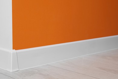 Photo of White plinth with connector on laminated floor near orange wall indoors
