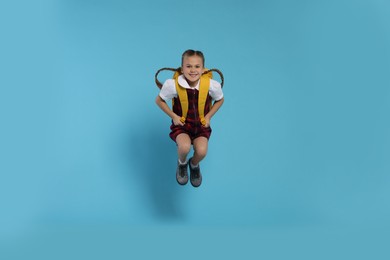 Photo of Happy schoolgirl with backpack jumping on light blue background