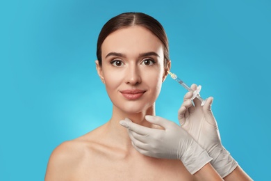 Beautiful woman getting facial injection on light blue background. Cosmetic surgery