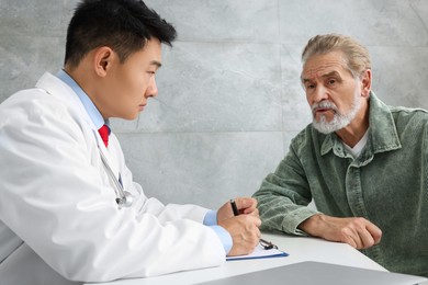 Photo of Doctor consulting senior patient at white table in clinic