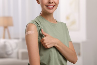Photo of Woman with sticking plaster on arm after vaccination showing thumbs up at home, closeup