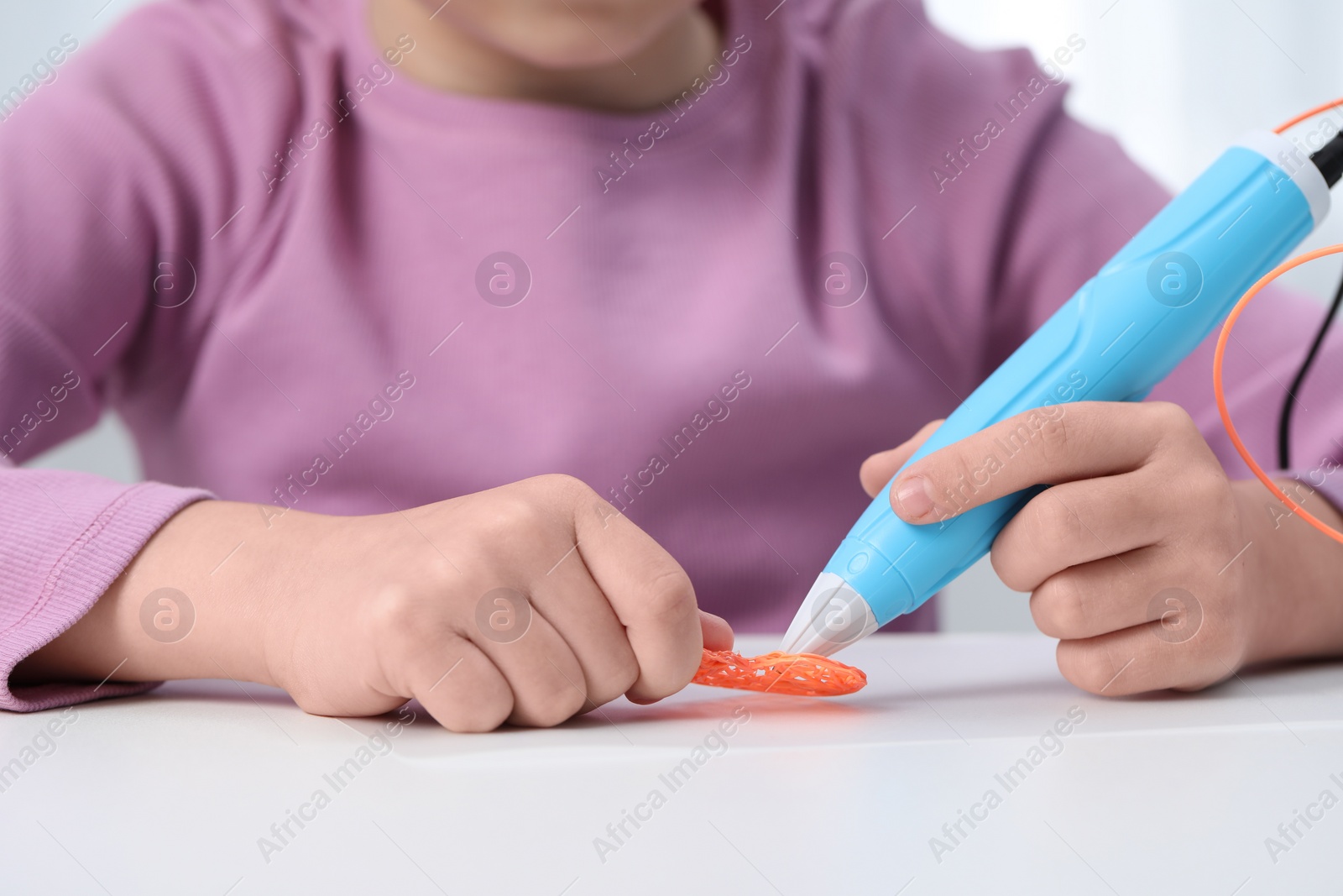 Photo of Girl drawing with stylish 3D pen at white table indoors, closeup