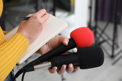 Professional journalist with microphones taking notes indoors, closeup