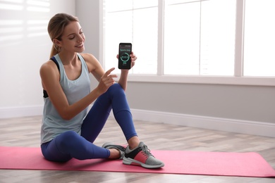 Photo of Young woman showing smartphone with fitness app indoors. Space for text