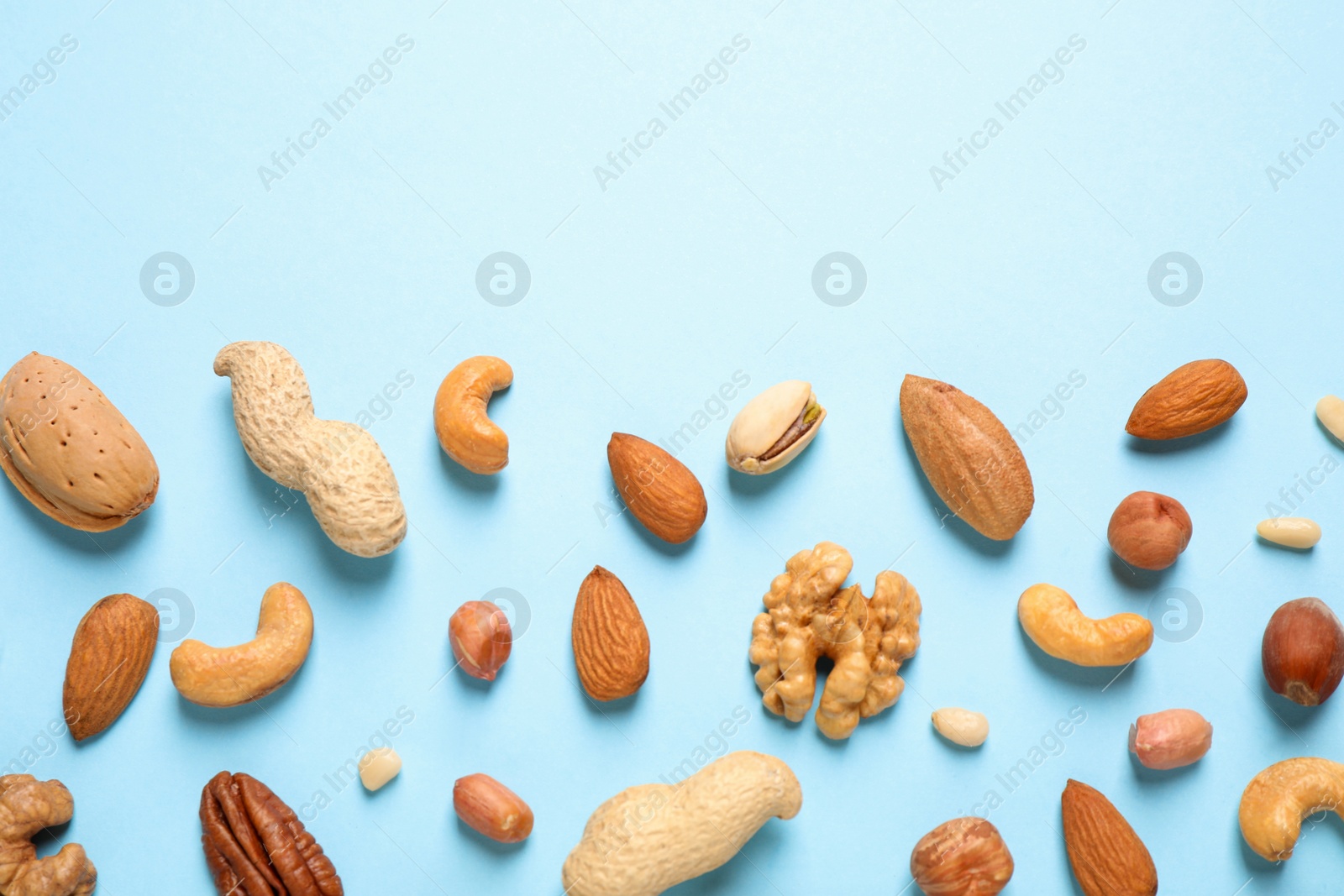 Photo of Different delicious nuts on light blue background, flat lay. Space for text