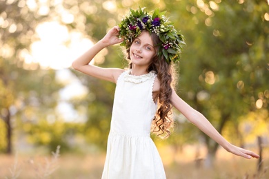 Photo of Cute little girl wearing wreath made of beautiful flowers outdoors on sunny day