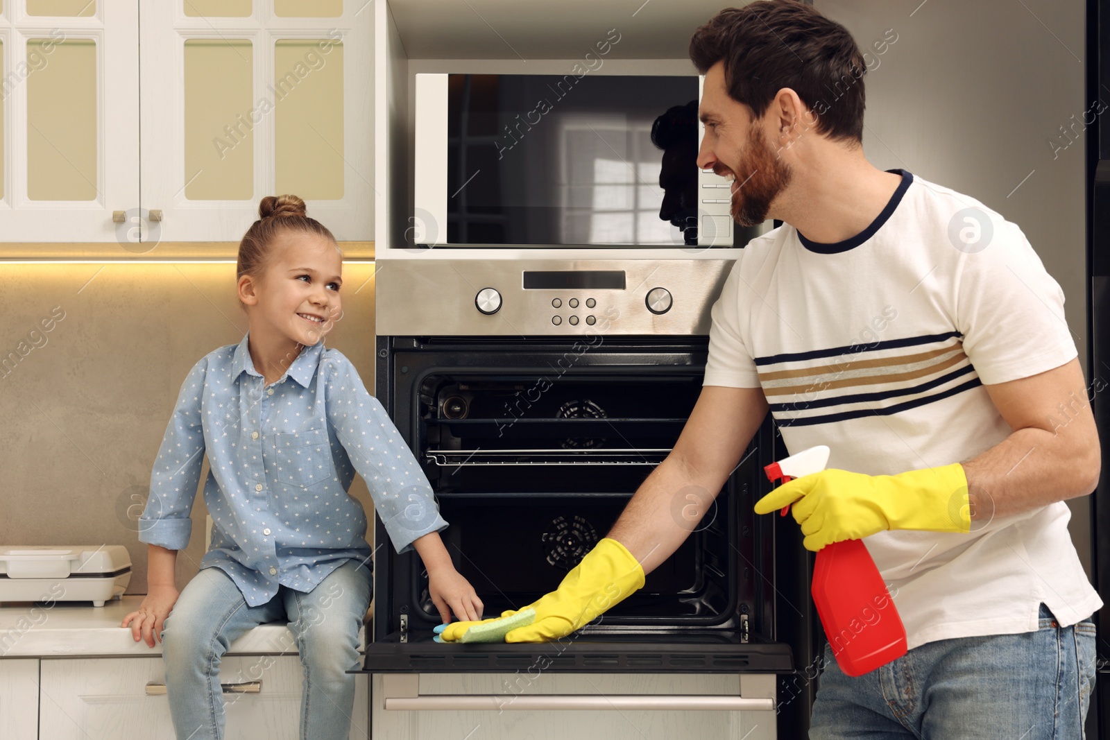 Photo of Spring cleaning. Father and daughter tidying up oven in kitchen together