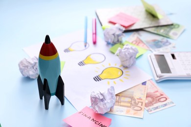 Photo of Composition with toy rocket and stationery on light blue background, space for text. Startup concept