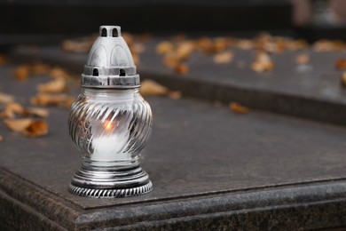 Photo of Grave lantern with burning candle on granite surface in cemetery, space for text