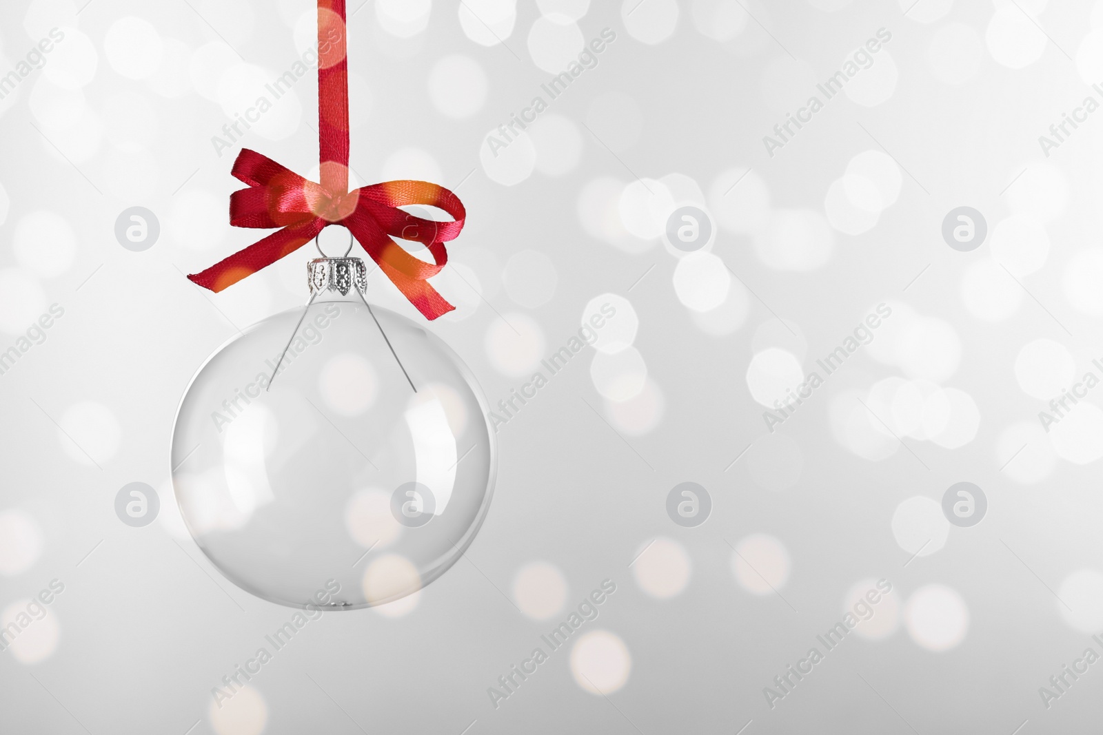 Photo of Transparent glass Christmas ball with red ribbon and bow against light background. Space for text