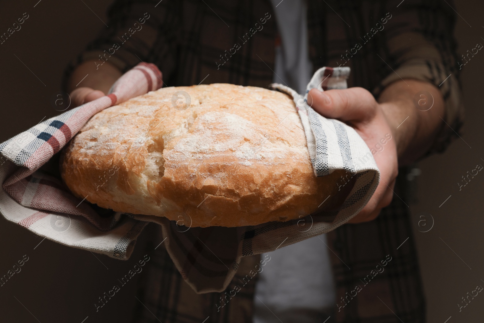 Photo of Man breaking loaf of fresh bread on dark background, closeup