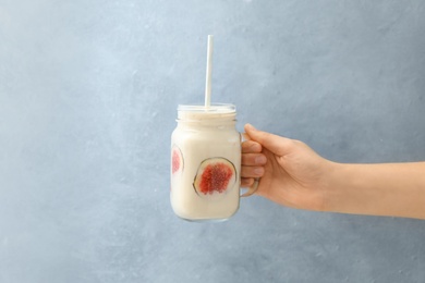 Woman holding mason jar with fig smoothie on light blue background, closeup