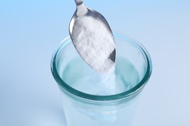 Photo of Adding baking soda into glass of water on light blue background, closeup