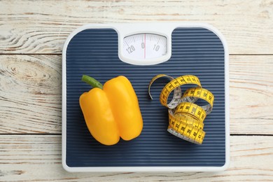 Photo of Scales with bell pepper and measuring tape on white wooden table, top view. Weight loss