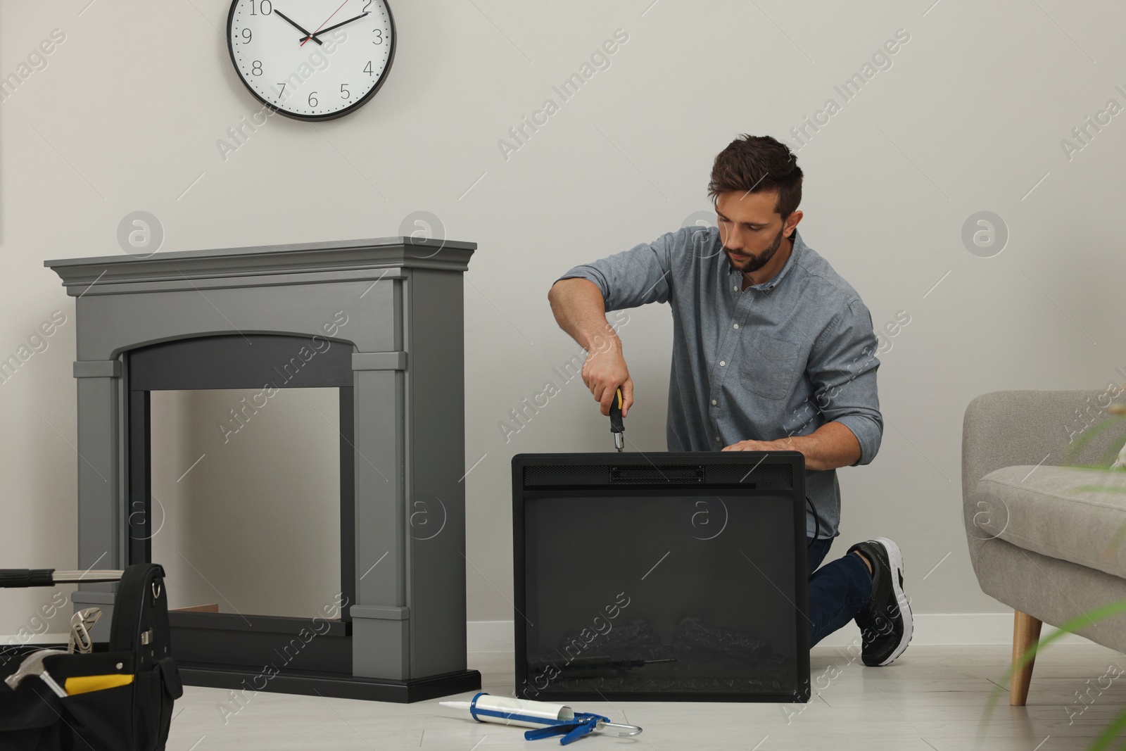 Photo of Man with screwdriver installing electric fireplace near wall in room