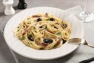 Photo of Delicious pasta with anchovies, olives and parmesan cheese served on grey table, closeup