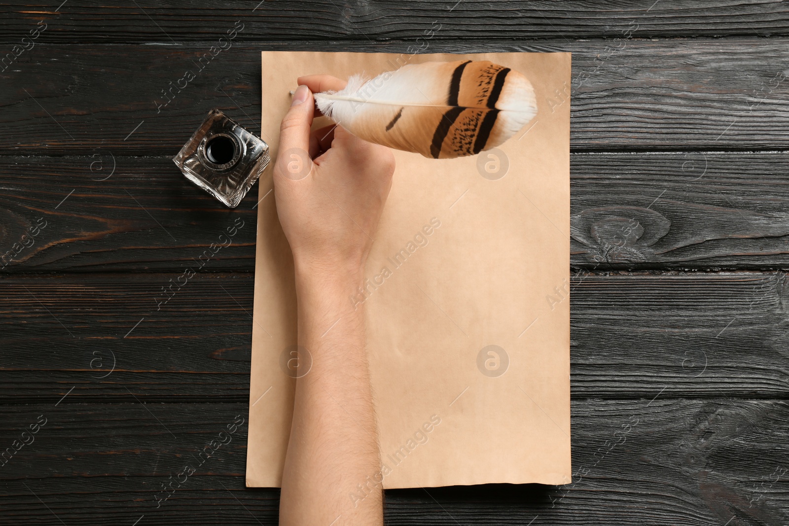 Photo of Woman using feather pen to write with ink on parchment at wooden table, top view. Space for text