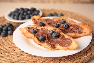 Photo of Tasty croissant with chocolate paste and blueberries on wicker mat