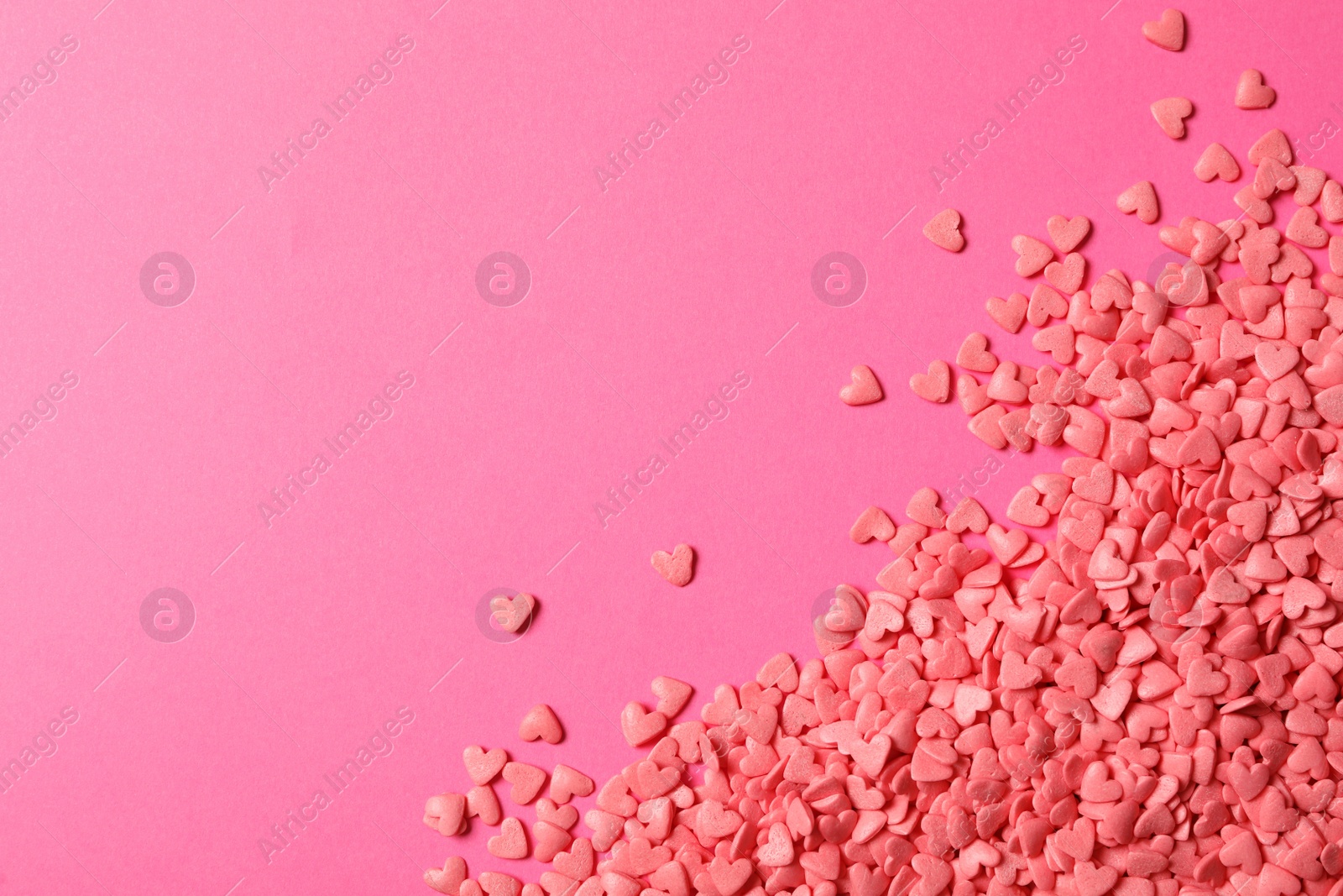 Photo of Heart shaped sprinkles on pink background, flat lay. Space for text