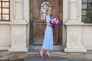 Photo of Beautiful woman with bouquet of spring flowers near building outdoors