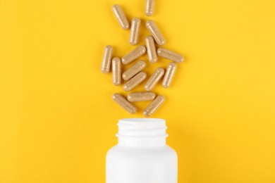 Photo of White medical bottle and vitamin capsules on yellow background, top view