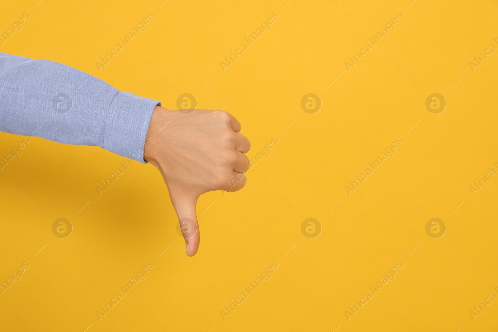 Photo of Man showing thumb down on orange background, closeup. Space for text