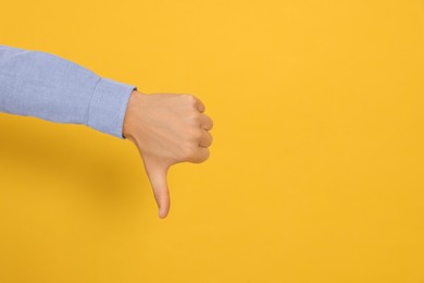Photo of Man showing thumb down on orange background, closeup. Space for text