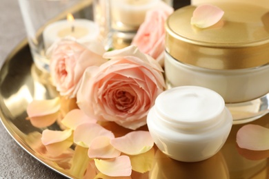 Photo of Composition with skin care products and roses on golden tray, closeup