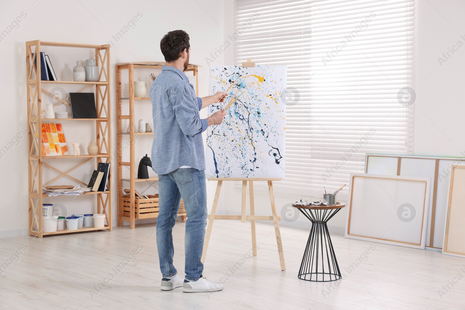 Photo of Man painting in studio, back view. Using easel to hold canvas