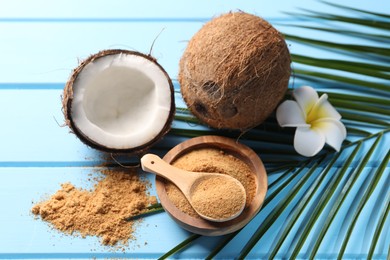 Coconut sugar, palm leaves, fruits and flower on light blue wooden table, above view