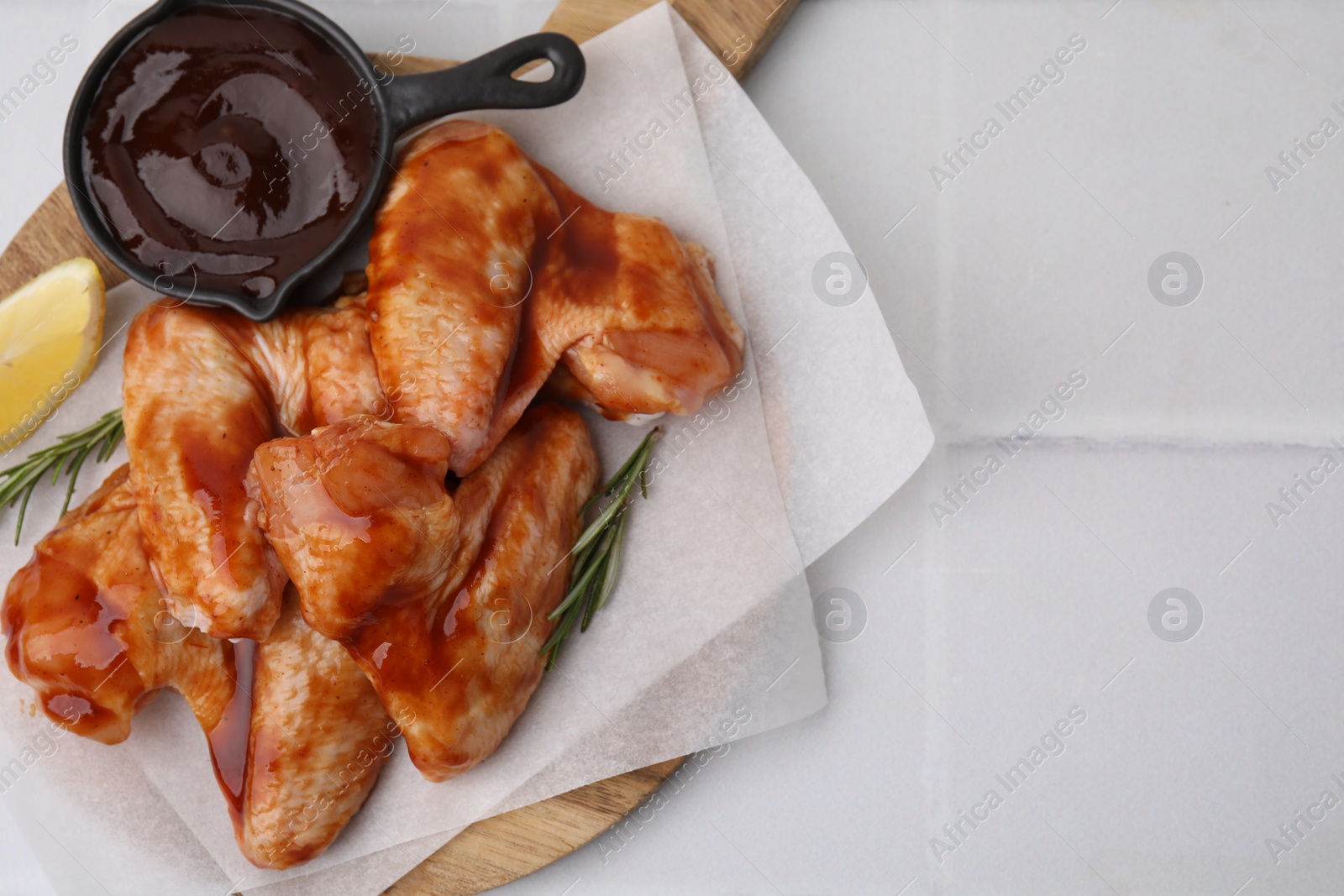 Photo of Raw chicken wings, rosemary, lemon and marinade on light tiled table, top view. Space for text