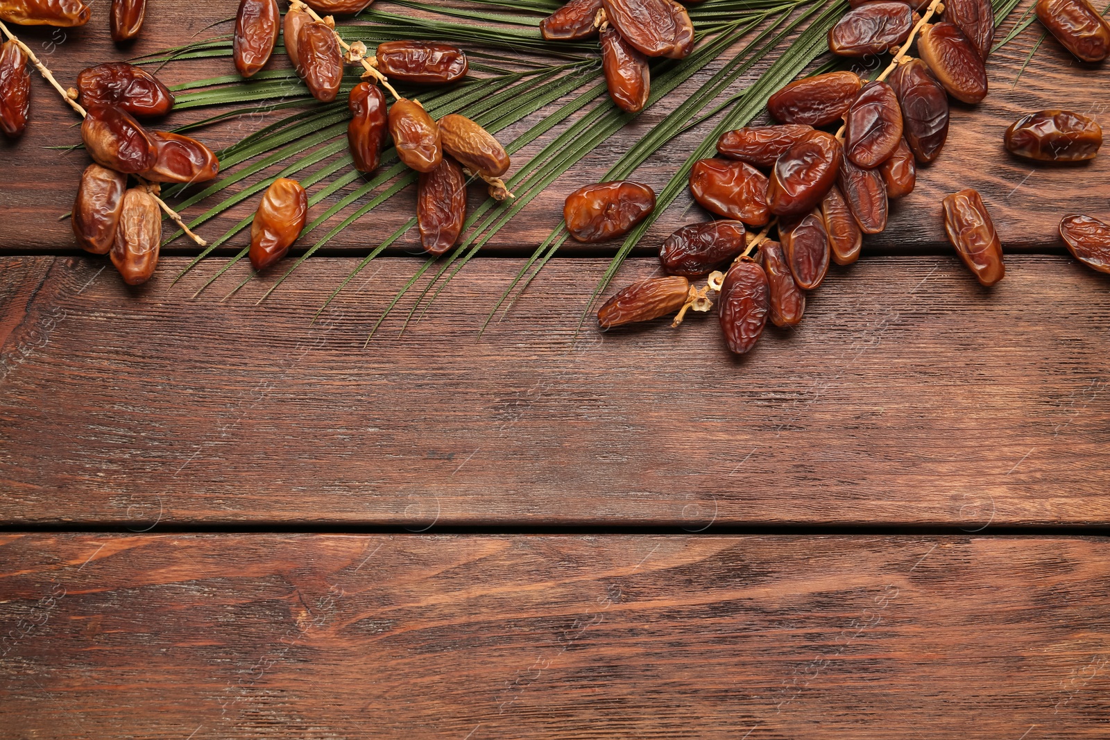 Photo of Branches with sweet dried dates and green leaf on wooden table, flat lay. Space for text