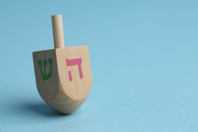 Wooden dreidel on light blue background, closeup with space for text. Traditional Hanukkah game