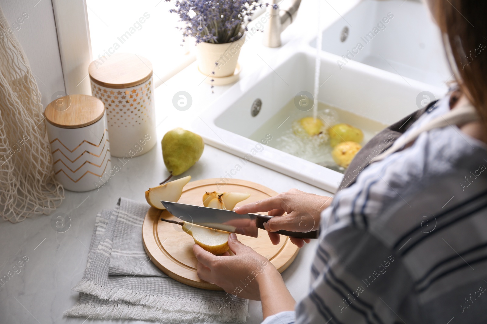 Photo of Woman cutting fresh ripe pear at table in kitchen, closeup