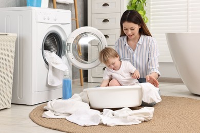 Photo of Happy mother with her daughter having fun while washing baby clothes in bathroom