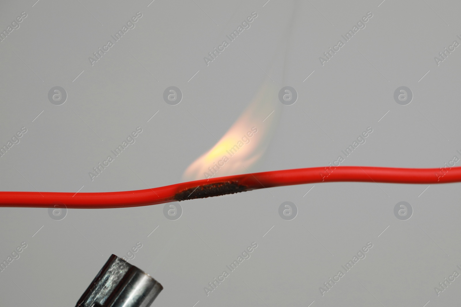 Photo of Inflamed red wire on grey background, closeup. Electrical short circuit