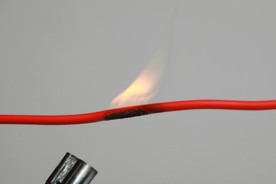 Inflamed red wire on grey background, closeup. Electrical short circuit