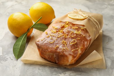 Photo of Wrapped tasty lemon cake with glaze and citrus fruits on light grey textured table